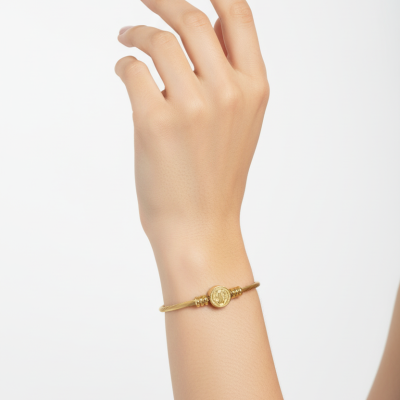 Pulseira dourada com fio torcido e elemento redondo ao centro no pulso