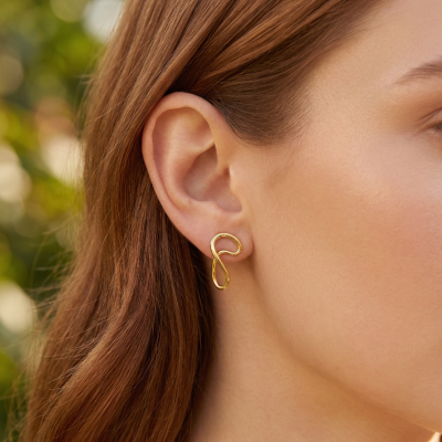 Brinco de pendente dourado em orelha de mulher com cabelo castanho aloirado.