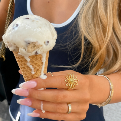Gelado creme com pedaços de chocolate em cone de waffle, mão feminina com unhas manicuras francesas e joias, fundo com mala preta e roupa azul.