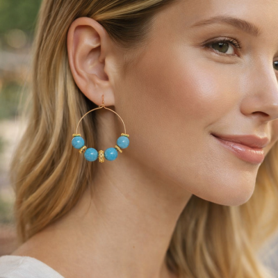 Brinco de argola dourado com contas azuis usado por mulher loira