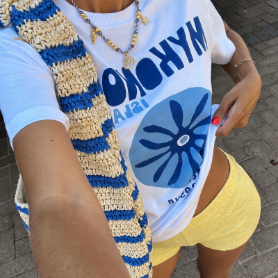 T-shirt branca com estampado azul, shorts amarelos, bolsa de malha azul e bege, colar com contas douradas e pendentes do mar