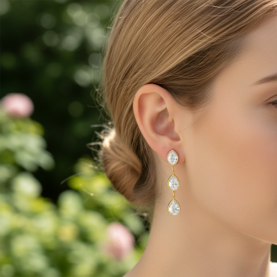 Brinco de ouro com três pedras transparentes em gota no ouvido de mulher