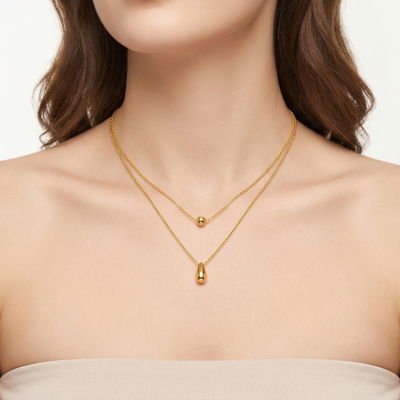 Colar duplo dourado com pendentes redondo e em gota num pescoço feminino