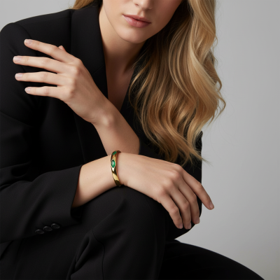 Pulseira dourada com pedras verdes no pulso de mulher com casaco preto