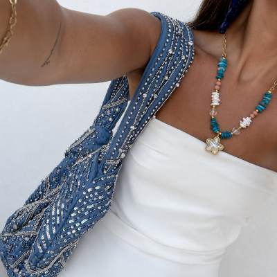 mala azul com lantejoulas e vestido branco com colar colorido e brincos azuis