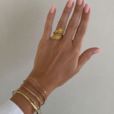 Mão com anel duplo dourado e pulseiras finas em fundo claro