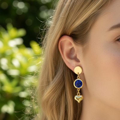 Brinco pendente dourado com pedra azul e coração dourado junto à orelha feminina.