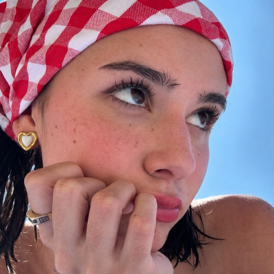 Pessoa com bandana vermelha e branca, brincos dourados de coração e anel prateado com detalhes pretos no dedo