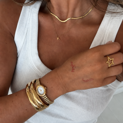 Mulher com pulseira dourada, relógio, colares e argola em forma de estrela em camisola branca