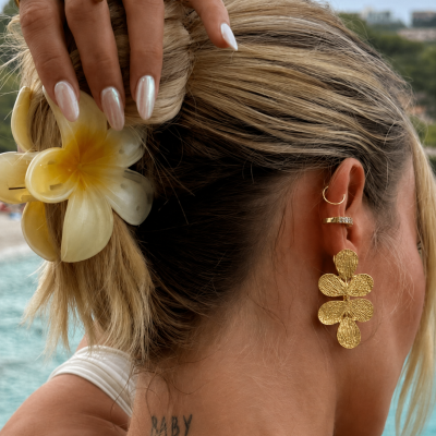 Pendentes dourados em forma de flor, anéis dourados e acessórios num cabelo loiro com flor amarela, vista traseira