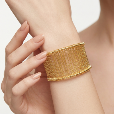 Pulseira dourada larga em pulso com unhas compridas nude