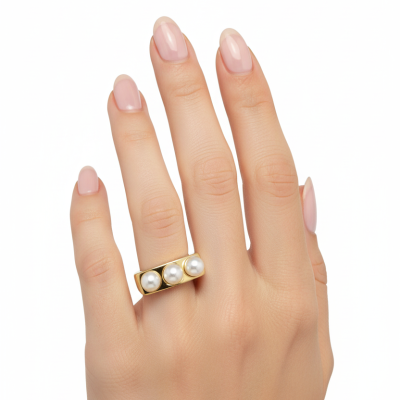 Anel dourado com três pérolas num dedo de mão com unhas naturais e fundo branco