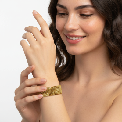 Pulseira de malha dourada larga no pulso de mulher com cabelo castanho ondulado e sorriso suave