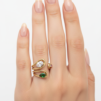 Mão feminina com unhas naturais e anel em ouro com pedras verdes e transparentes