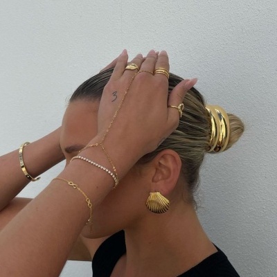 Mulher com acessórios dourados e cabelo preso em coque, fundo branco