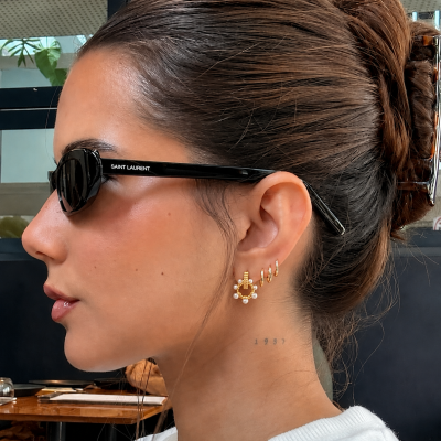Óculos de sol pretos Saint Laurent em modelo feminino com brincos dourados e tatuagem no pescoço