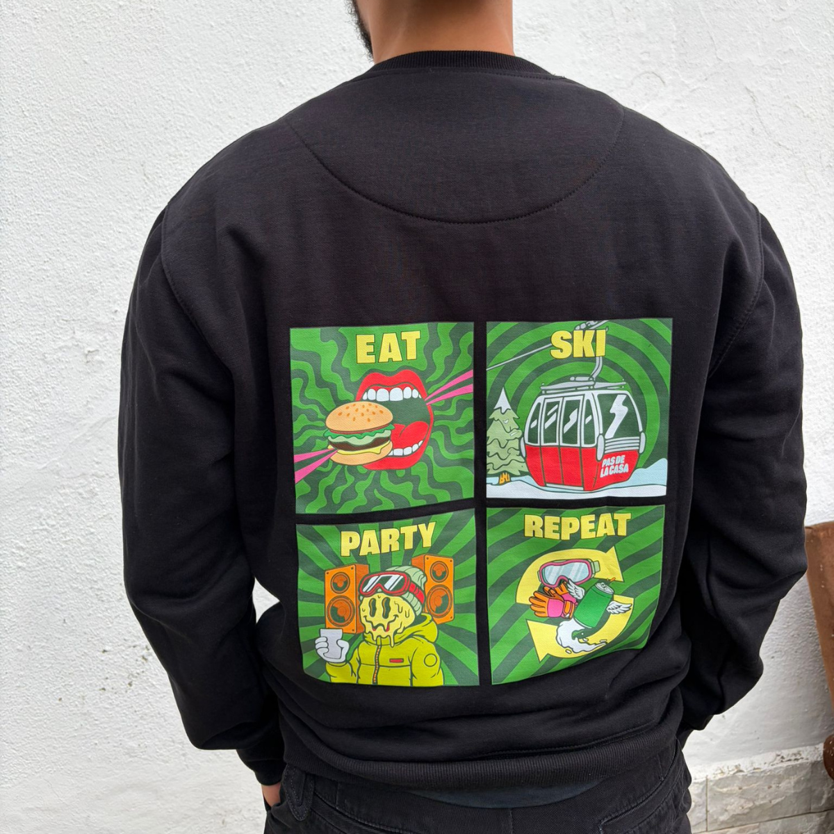Sweatshirt preta com estampado colorido e texto relacionado a comer, esquiar, festa e repetir.
