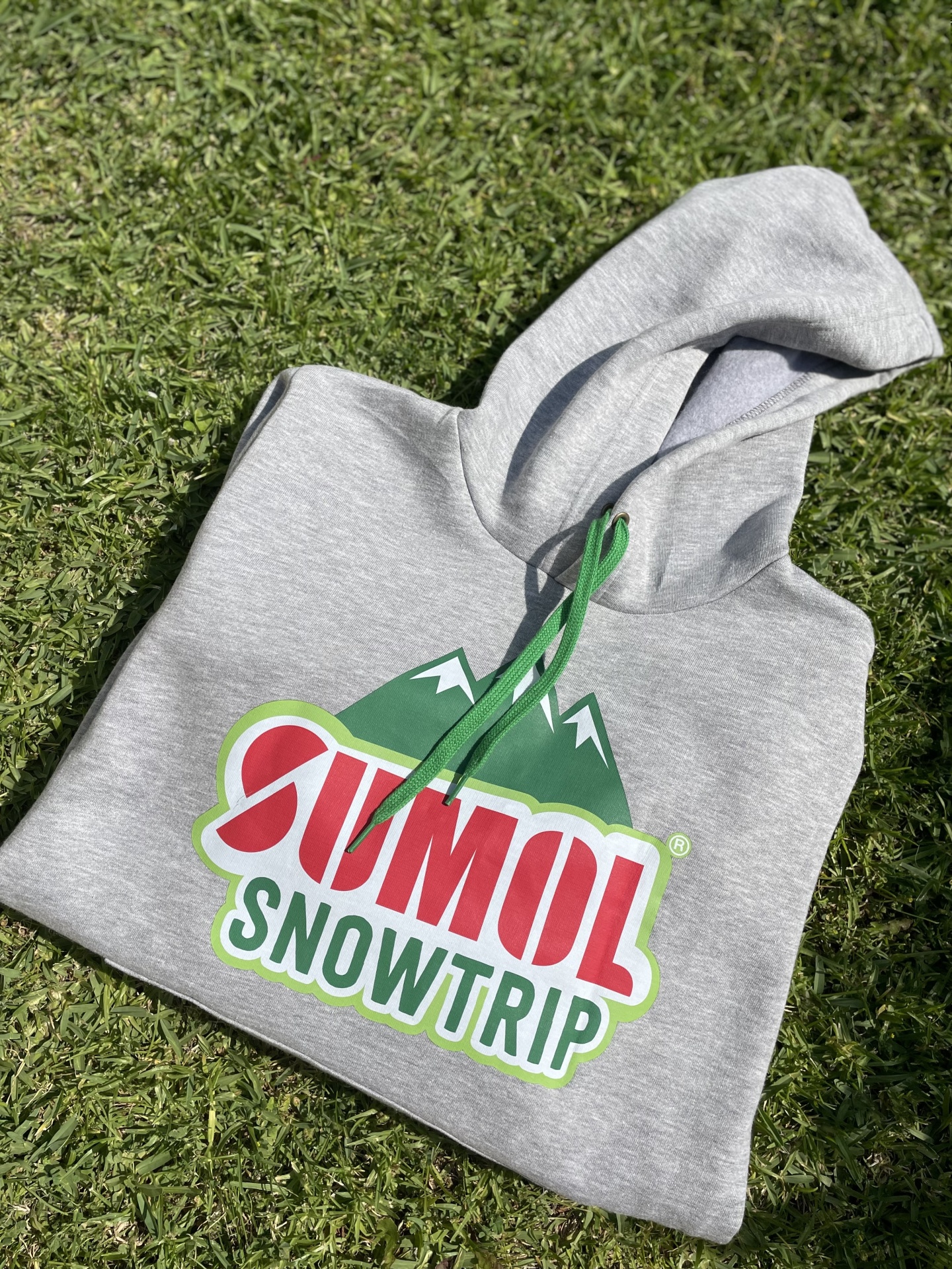Sweatshirt cinzenta com logotipo colorido SUMOL SNOWTRIP sobre relva