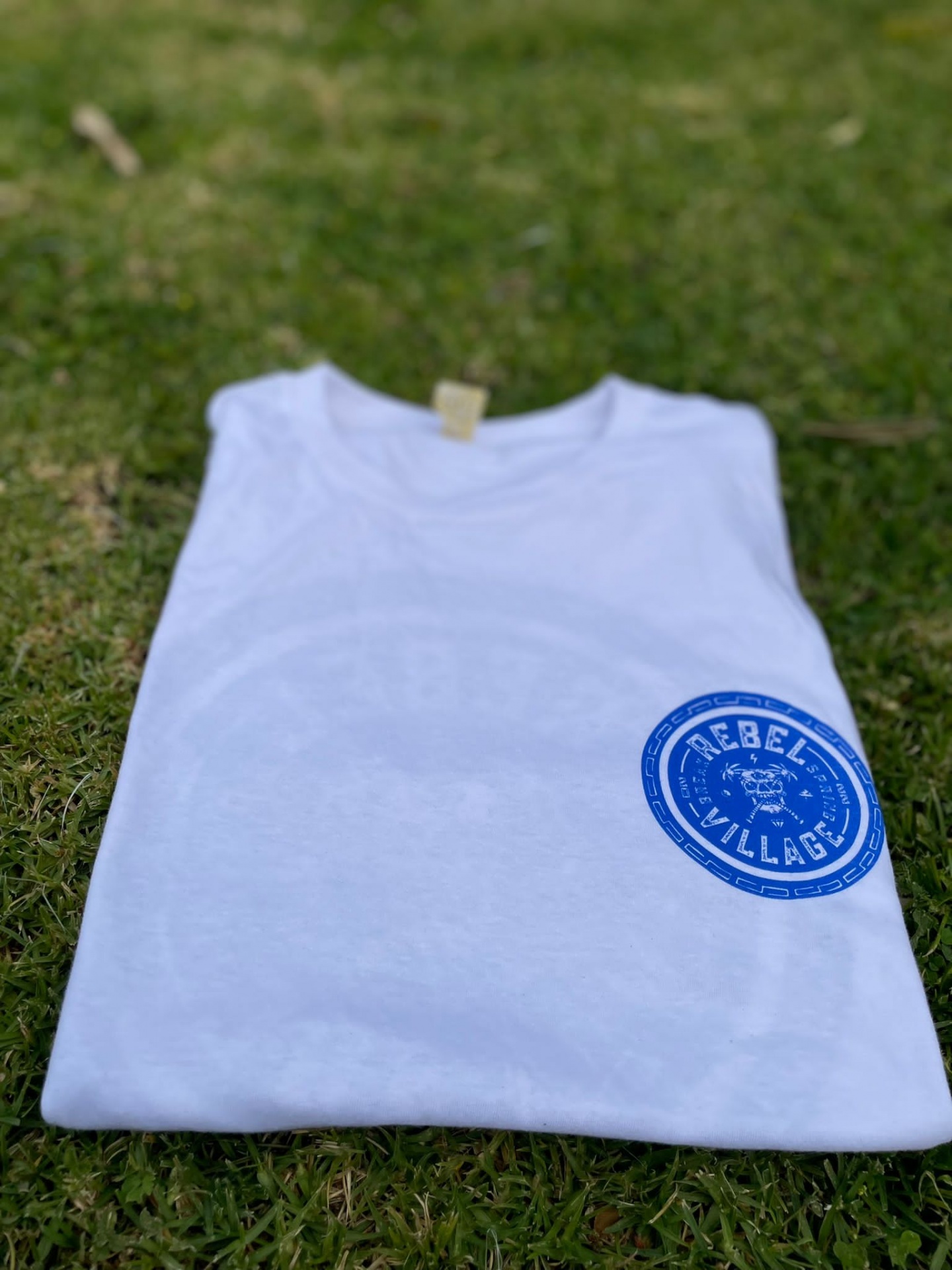 Camiseta branca com estampado azul REBEL VILLAGE sobre relva