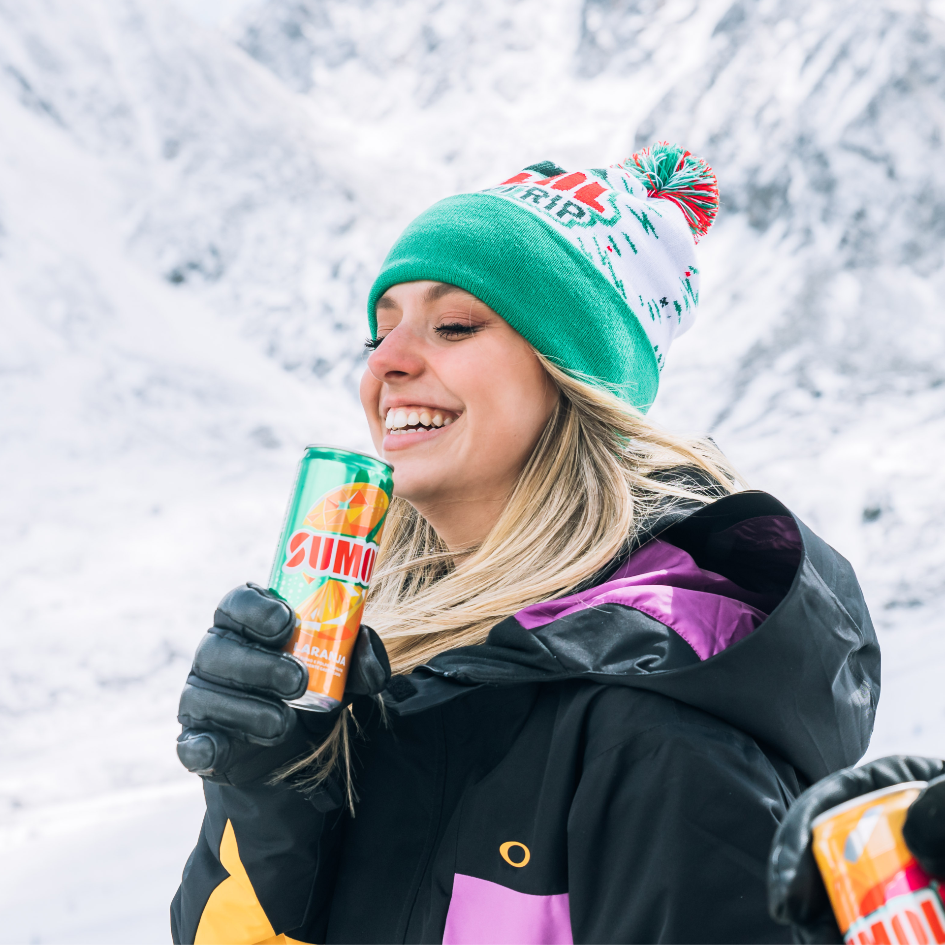 Mulher com casaco de inverno e gorro segurando lata de bebida SUMO em montanha nevada