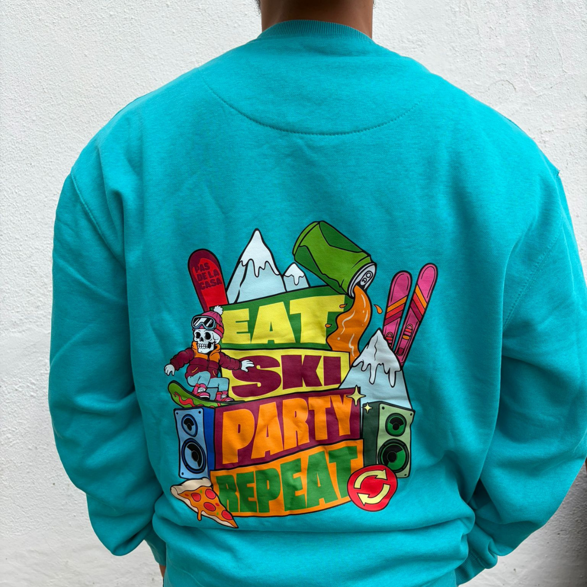 Casaco azul turquesa com estampa colorida e texto EAT SKI PARTY REPEAT