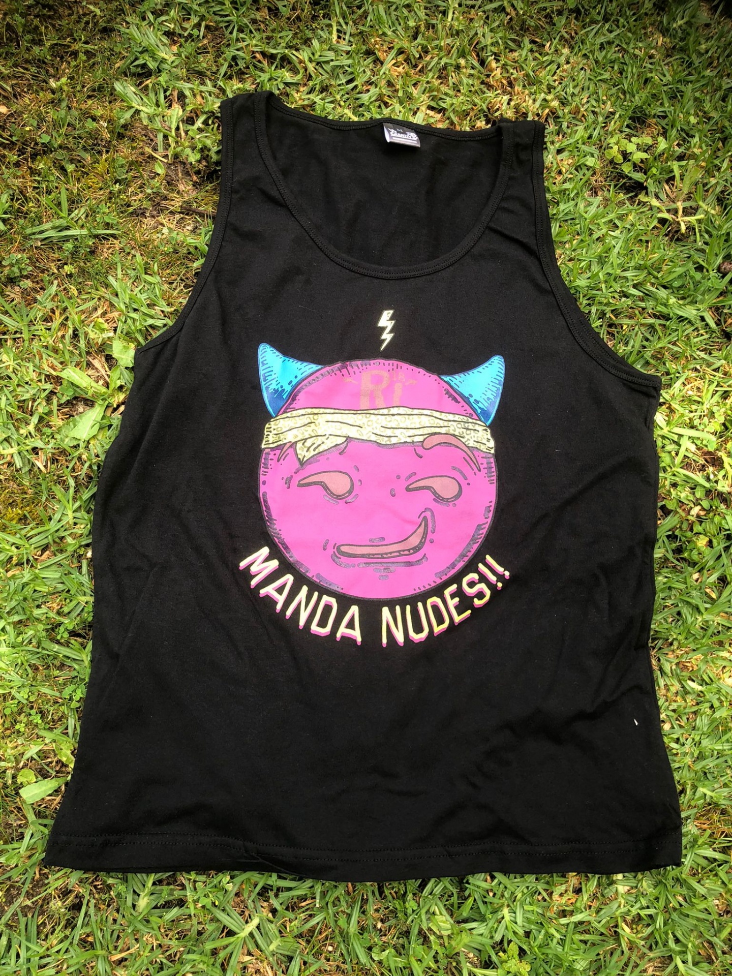 tank top preto com estampa colorida e texto MANDA NUDES!! sobre relva verde