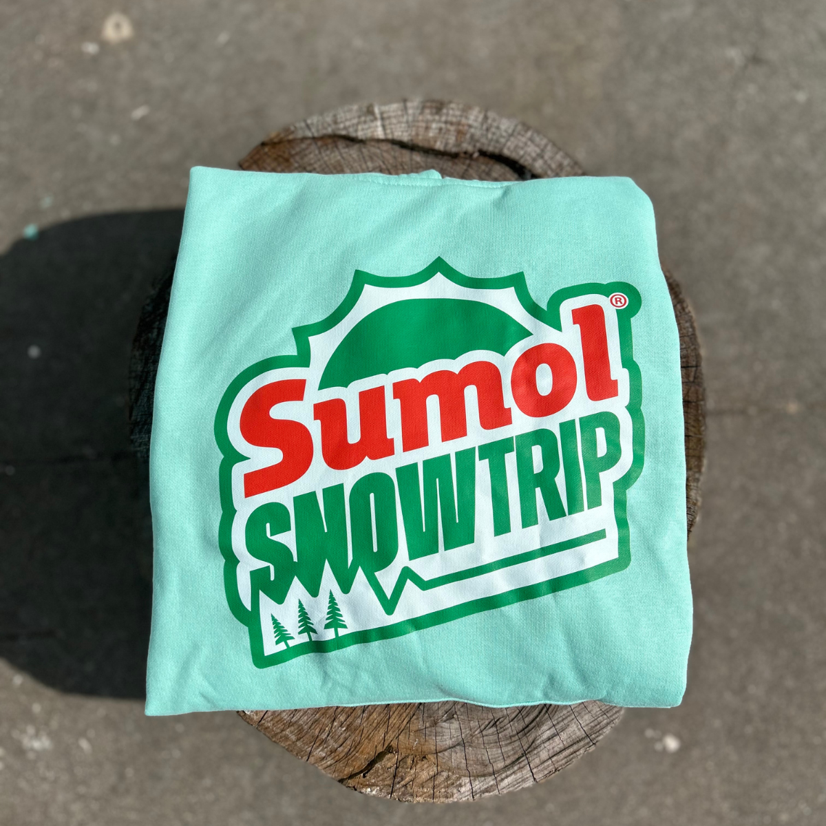 Camisola verde água com estampa Sumol SNOW TRIP sobre superfície de madeira