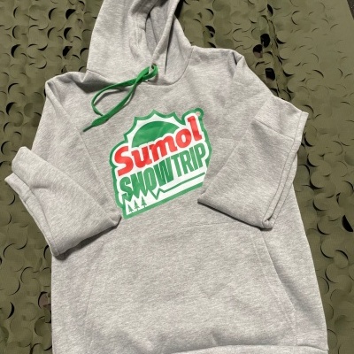 Camisola cinzenta com capuz e cordão verde, estampa 'SUMOL SNOWTRIP' com árvores sobre tecido verde recortado.