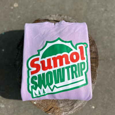 Camisola cor-de-rosa com estampa Sumol SNOWTRIP verde e vermelho sobre tronco de madeira