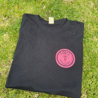 T-shirt preta com logótipo cor de rosa 'REBEL VILLAGE' sobre relva