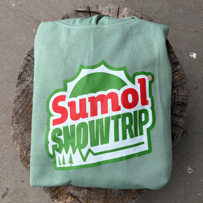 Sweatshirt verde claro com estampado Sumol SNOW TRIP sobre tronco de madeira.