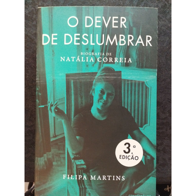 Capa do livro O Dever de Deslumbrar com imagem de mulher sentada e texto em azul e branco