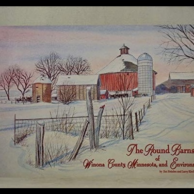 Capa de livro com celeiros redondos nevados e texto vermelho.