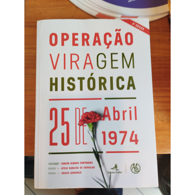 Capa de livro branco com letras vermelhas e verdes, e uma flor vermelha colocada sobre a capa, em cima de mesa de madeira
