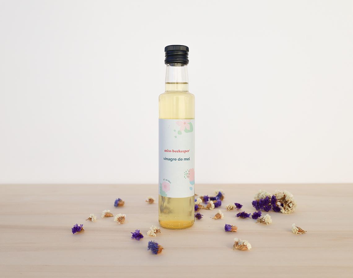 Frasco de vidro com vinagre de mel e flores secas numa mesa de madeira