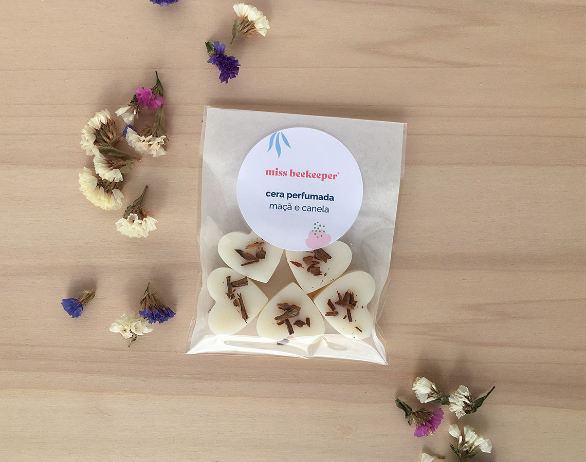 Pacote de corações de cera perfumada em embalagem transparente com etiqueta e flores secas ao redor.