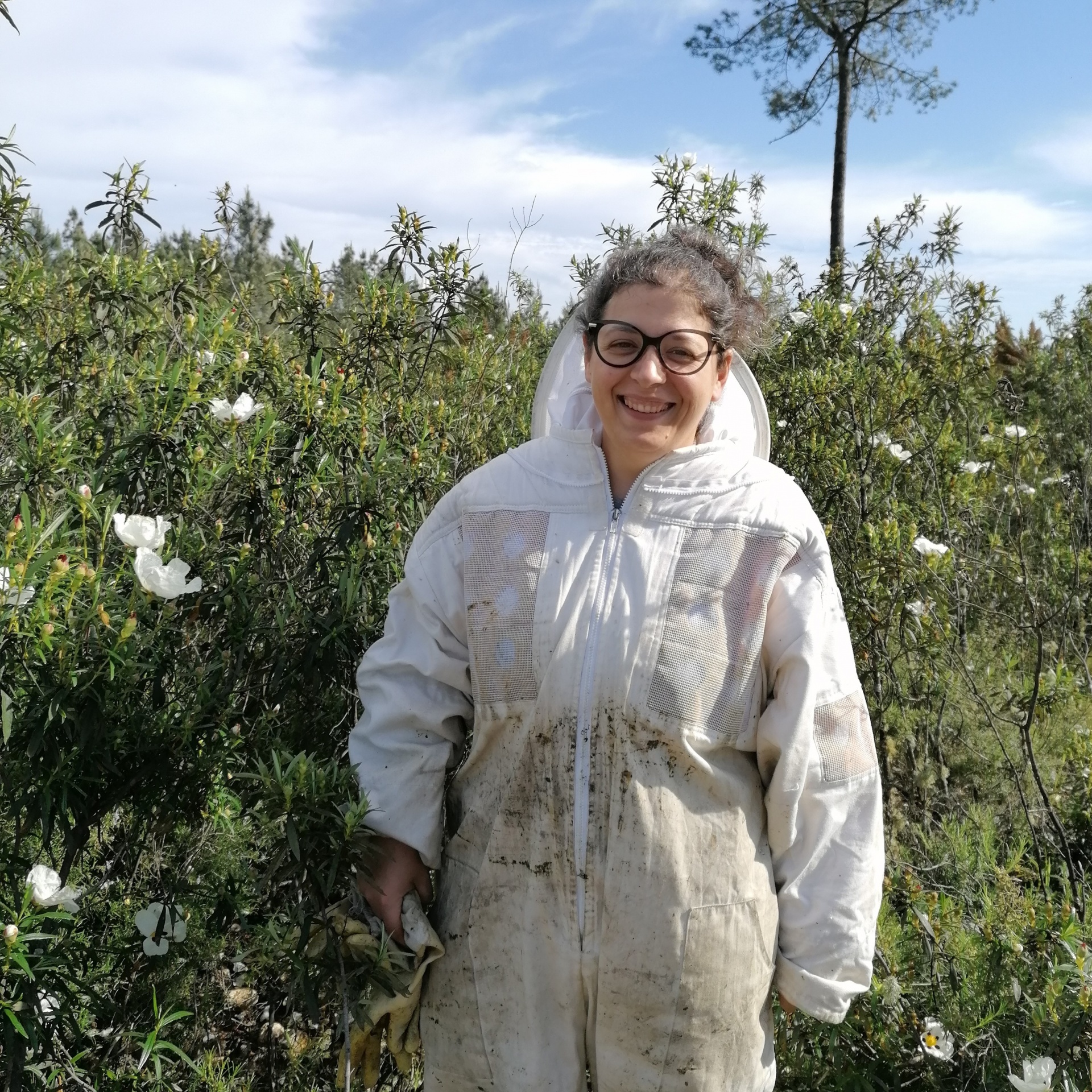 Pessoa com fato de proteção branco sujo e óculos ao ar livre junto a vegetação