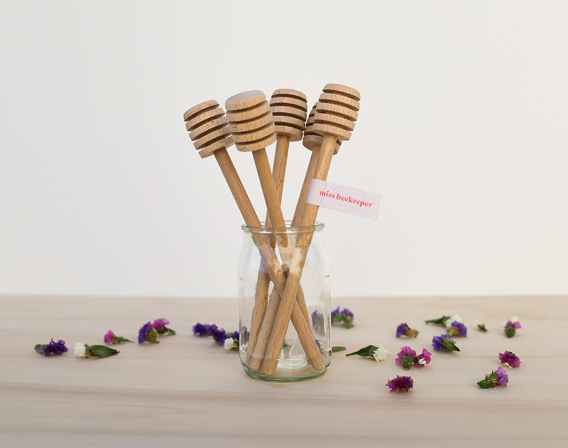 Colheres de mel de madeira em frasco de vidro com flores ao redor