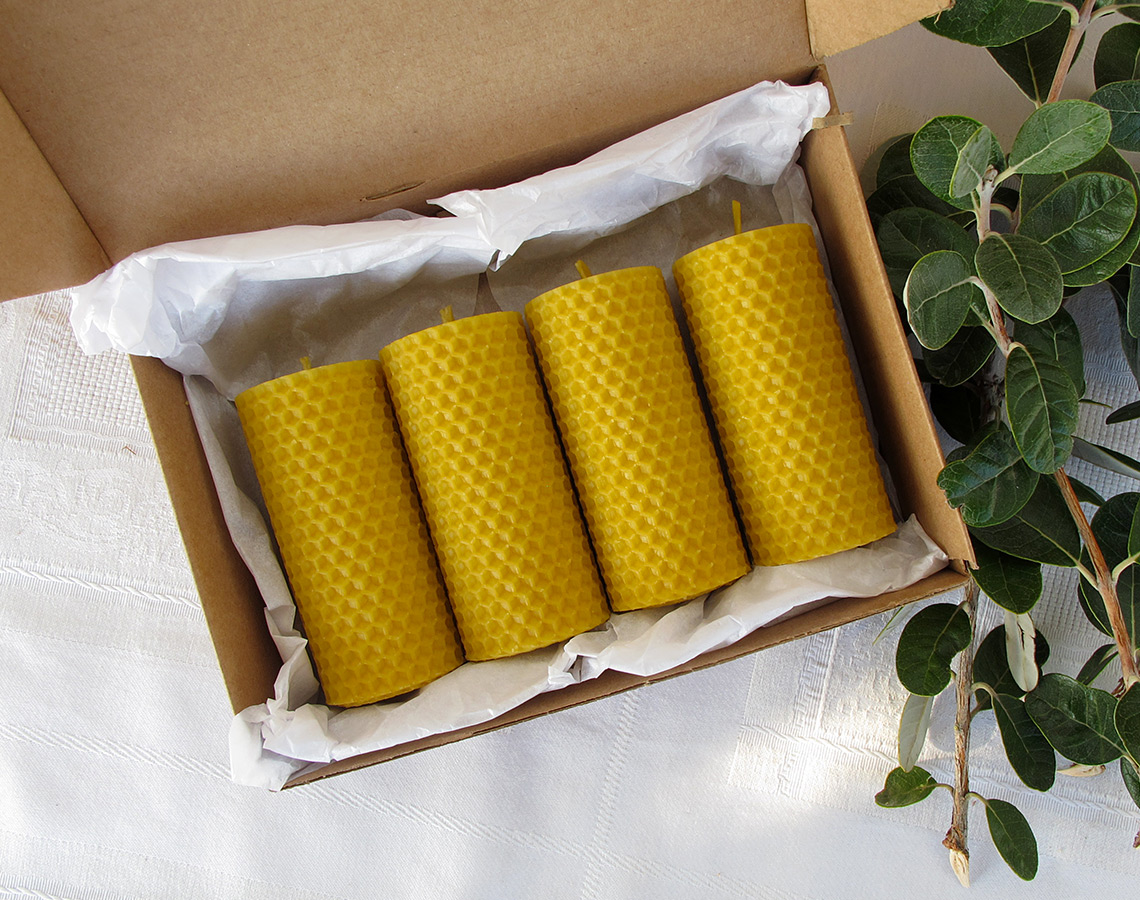 Caixa aberta com quatro velas amarelas texturizadas e um ramo verde ao lado