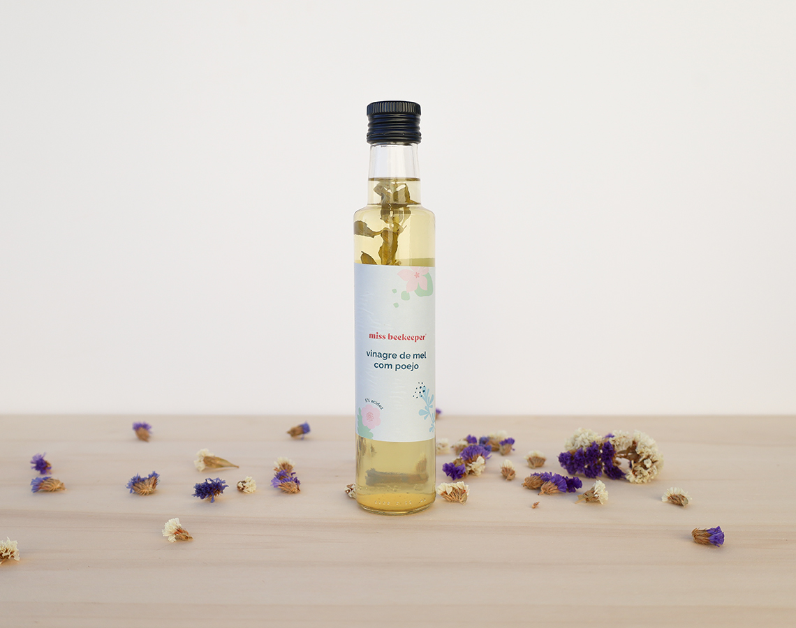 Garrafa de vidro com líquido amarelo e rótulo branco sobre mesa de madeira com flores secas ao redor