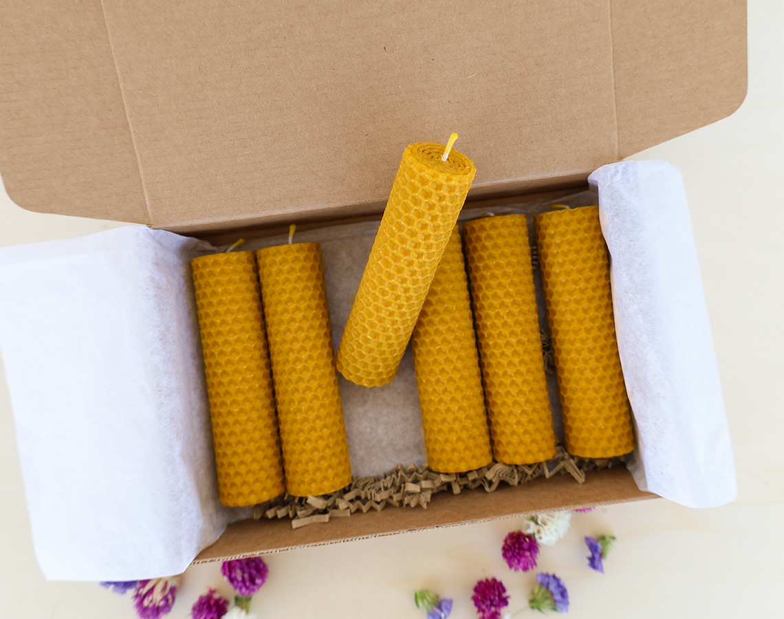Sete velas amarelas de cera de abelha numa caixa de cartão com flores secas ao redor