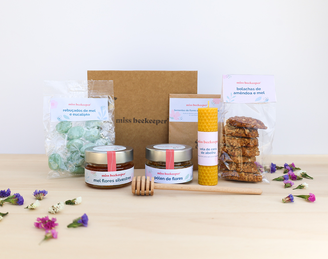 Produtos artesanais de mel e cera de abelha embalados em sacos transparentes e caixa de papelão sobre mesa de madeira clara