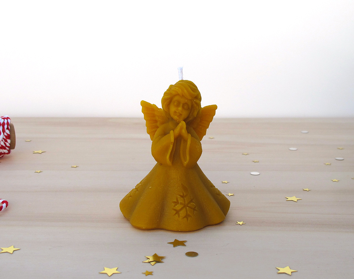 Vela em forma de anjo amarelo mostarda sobre mesa de madeira com confetis dourados e prateados