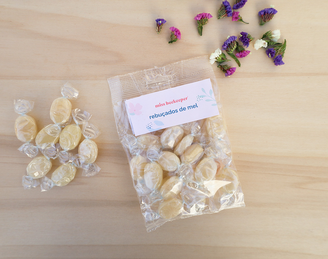 Pacote plástico de rebuçados de mel com rebuçados fora do pacote e flores coloridas ao lado