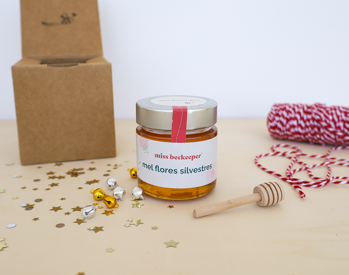 Frasco de mel com etiqueta branca, colher de mel de madeira, linha vermelha e branca e caixa de cartão castanho