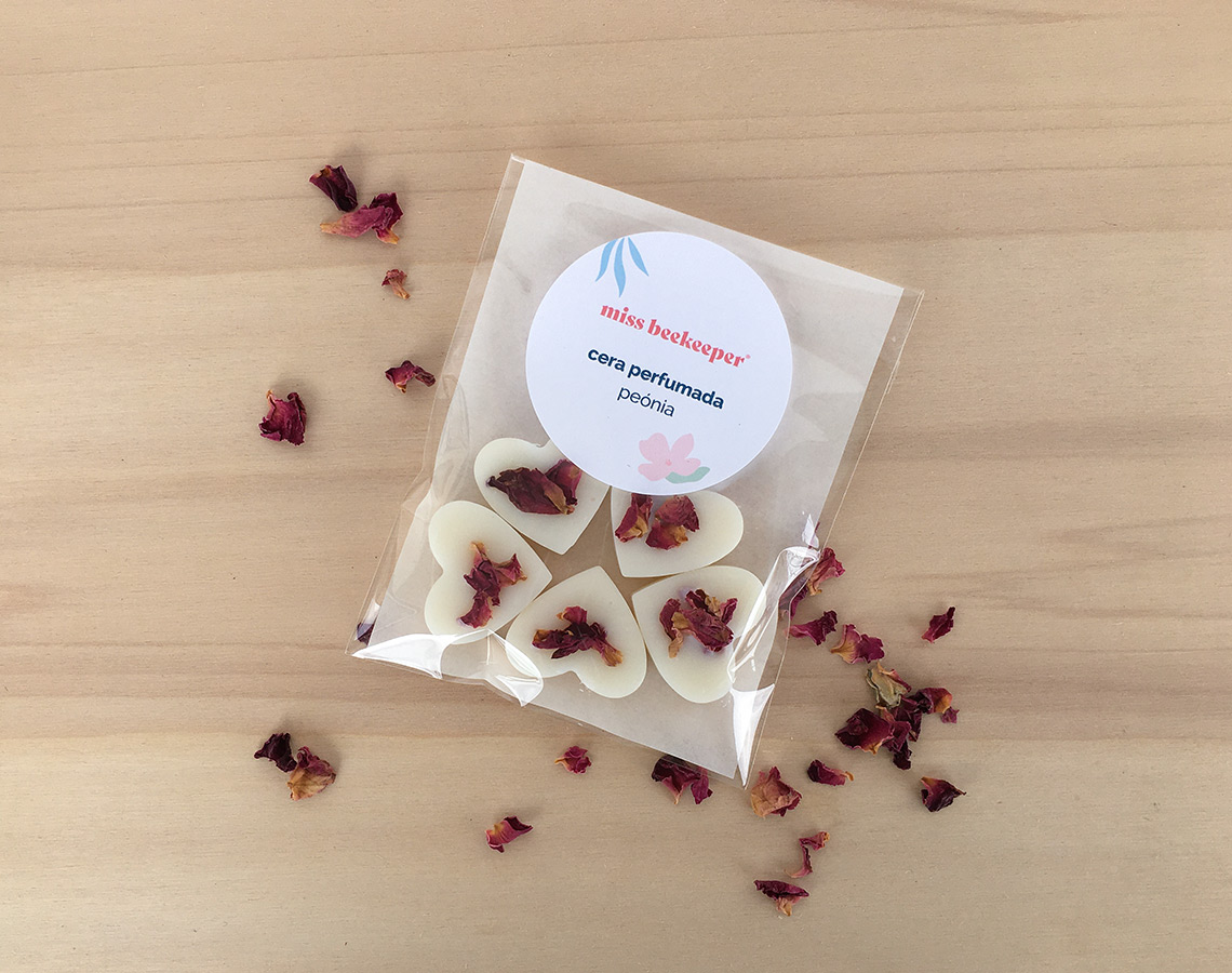 Pacote de velas perfumadas em forma de coração com pétalas de rosa, sobre mesa de madeira clara