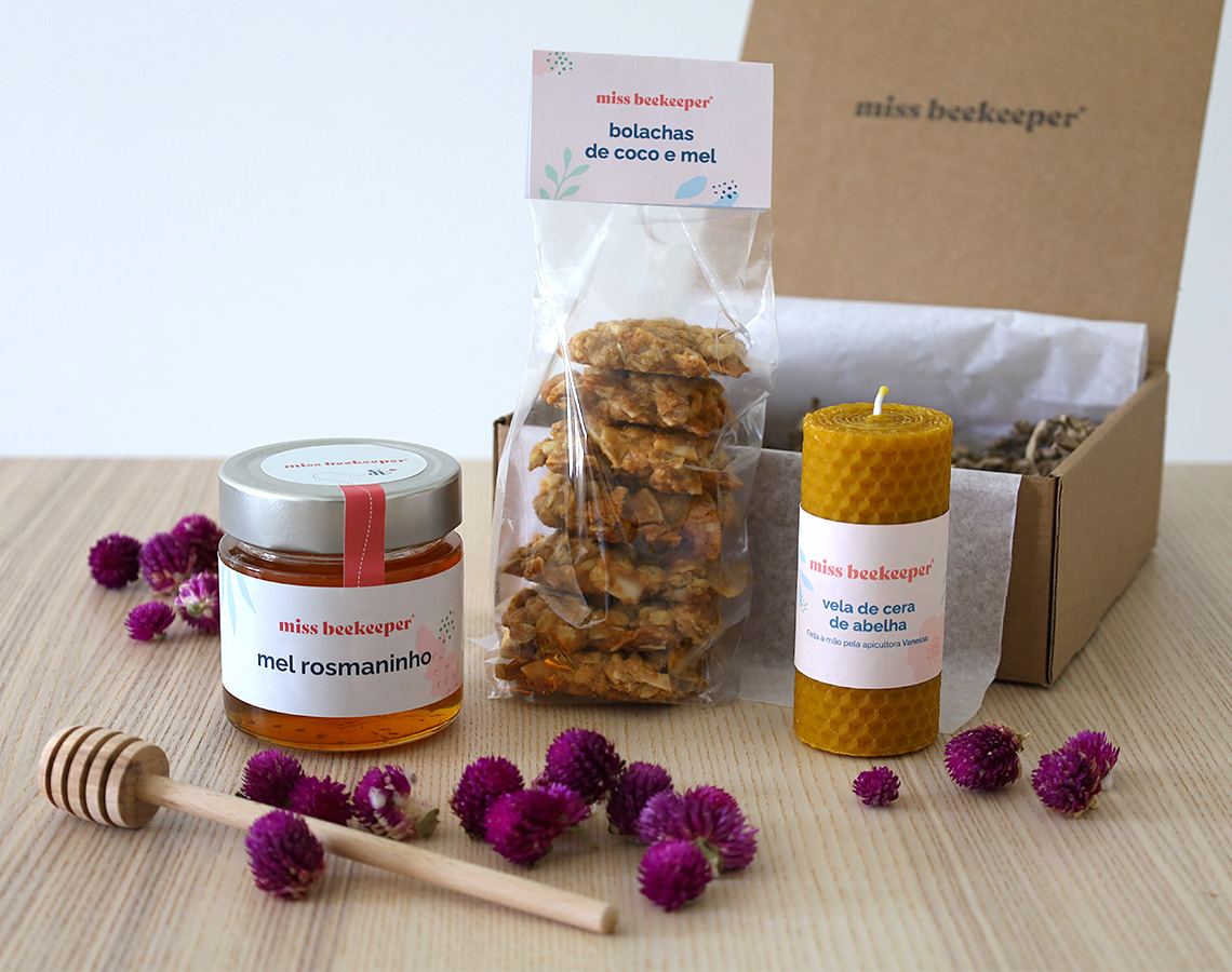 Conjunto de mel, bolachas de côco e mel, vela de cera de abelha e espalhador de mel sobre superfície madeira com flores lilases