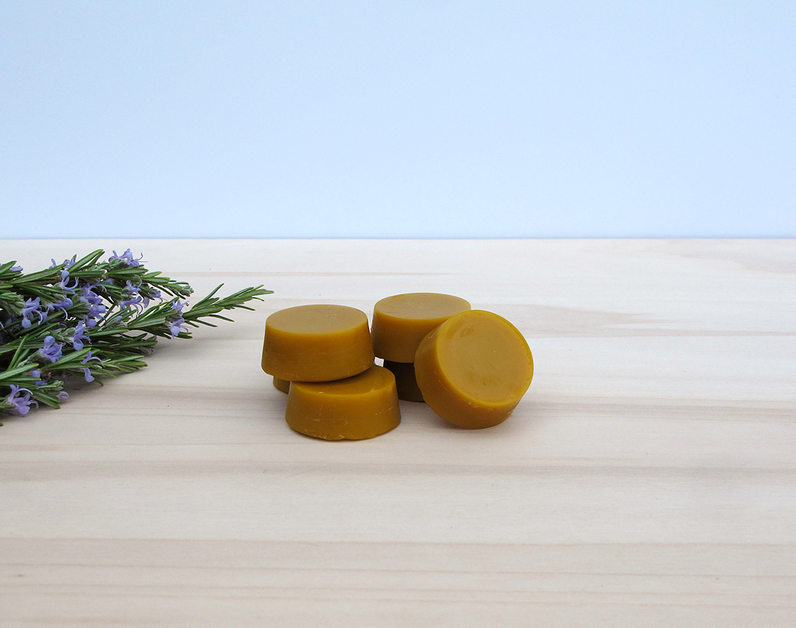 Quatro sabonetes castanhos claros sobre madeira clara com ramo de lavanda à esquerda