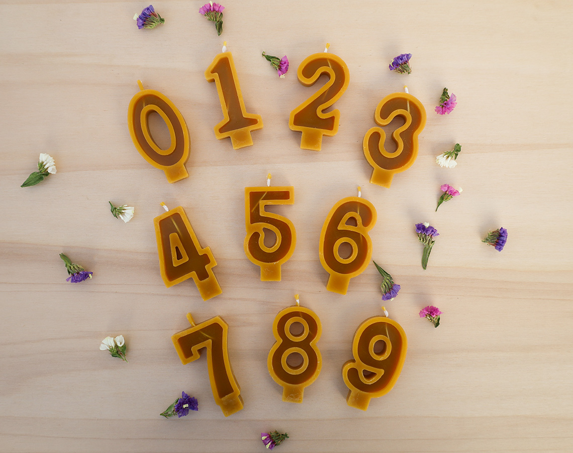 Velas em forma de números castanhos com bordas amarelas sobre madeira clara com flores