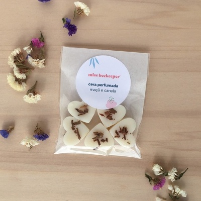 Pacote de corações de cera perfumada em embalagem transparente com etiqueta e flores secas ao redor.